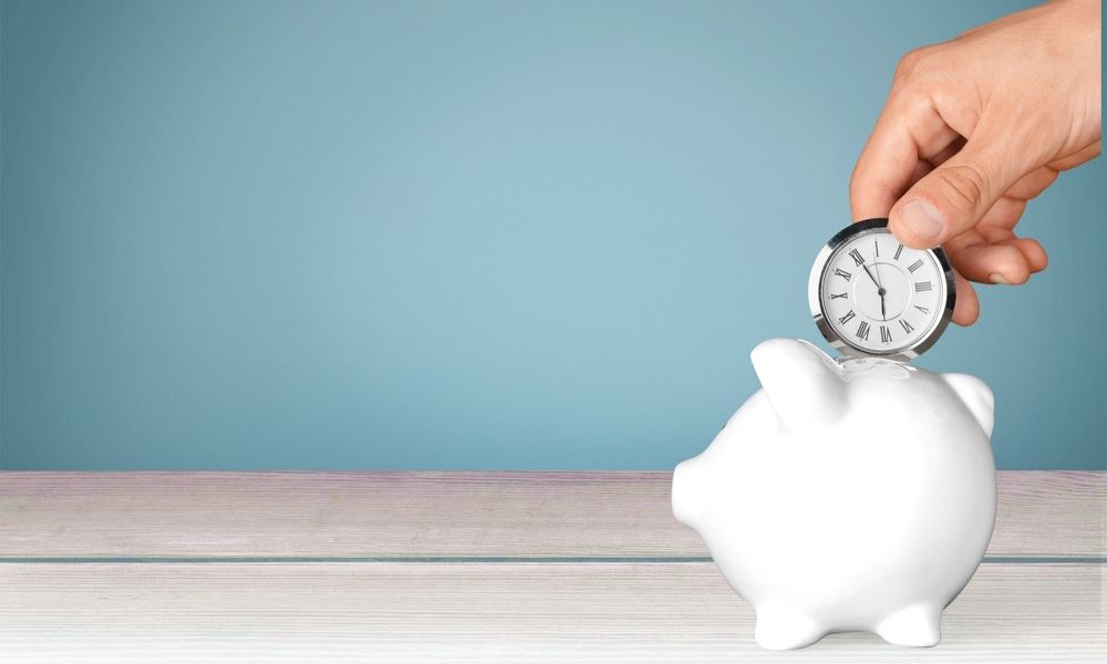 A hand-held timepiece is placed into the money slot of a piggybank