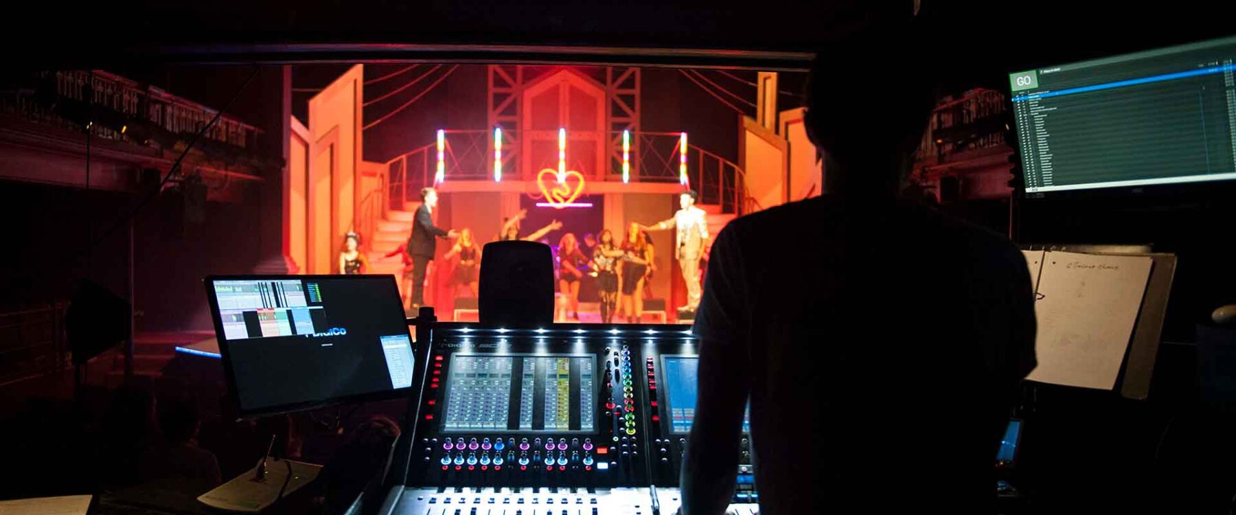 Mixing desk operator at the desk in front of a theatre production
