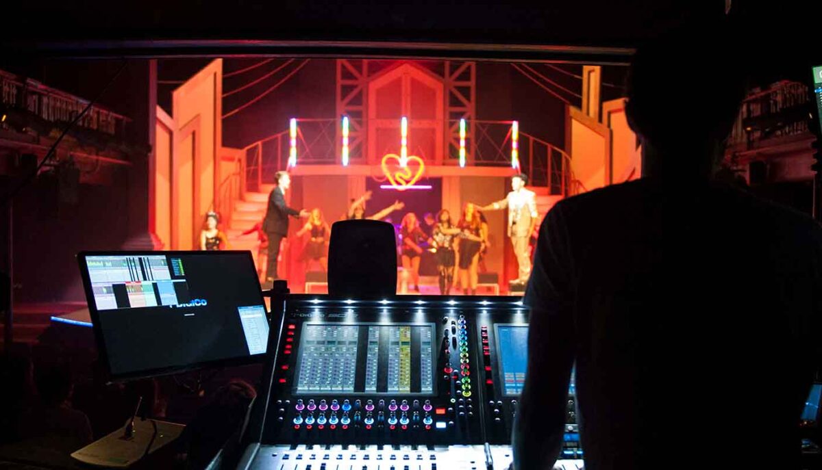 Mixing desk operator at the desk in front of a theatre production